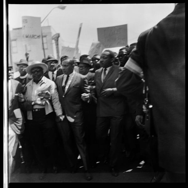 In 1968, union leader T.O. Jones organized Memphis sanitation workers into a strike demanding better pay and safer working conditions. After the city refused their requests, the workers began near-daily protests as trash piled up across Memphis for more than a month. By March, their pleas reached Dr. Martin Luther King Jr., who traveled to Memphis to lead a massive demonstration. Far larger than previous marches, this one quickly dissolved into chaos. Fearing for his safety and that of his aides, Dr. King was escorted away, though he vowed to return and lead a truly peaceful march. Tragically, when he came back to Memphis in early April to fulfill that promise, he was assassinated before he could lead the march. Here we see Dr. King being evacuated from the chaotic demonstration.